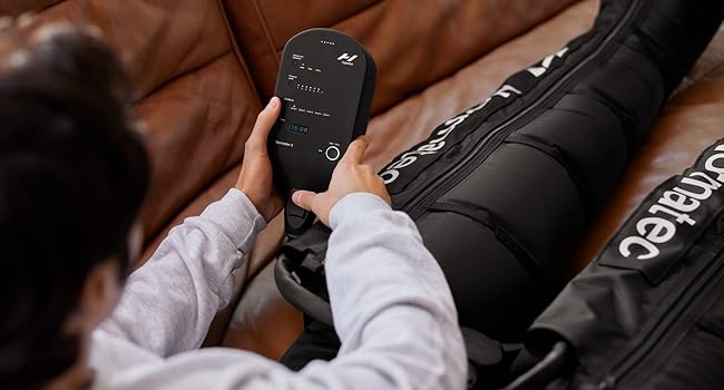 Man on a leather couch using a Normatec control unit.