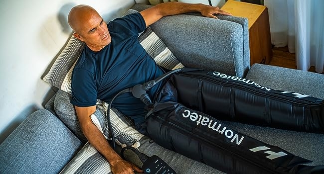 Kelly Slater sitting on a couch wearing Normatec boots.
